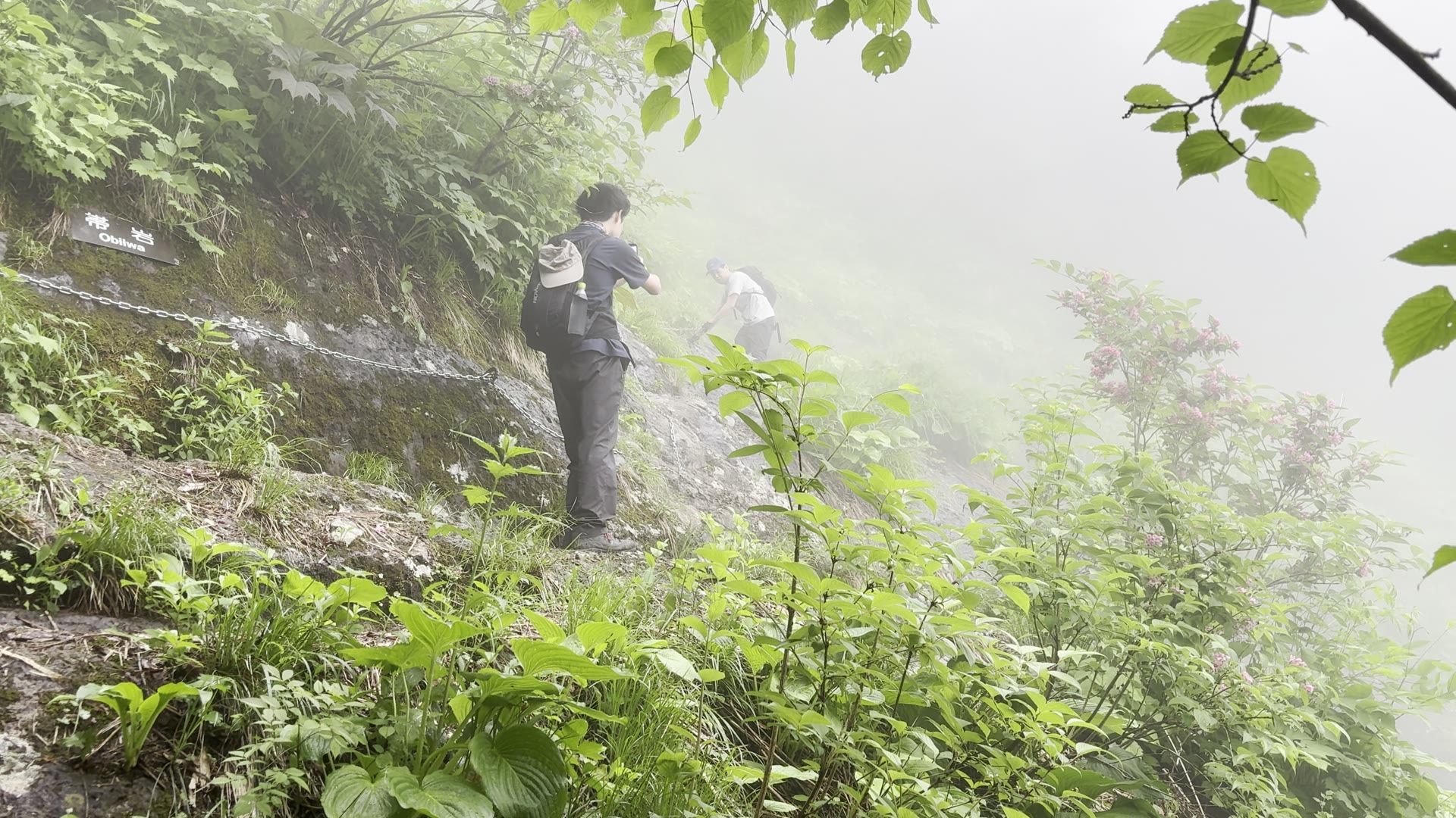 高妻山・帯岩のトラバース。霧の中、鎖を頼りに岩壁を横切る登山者
