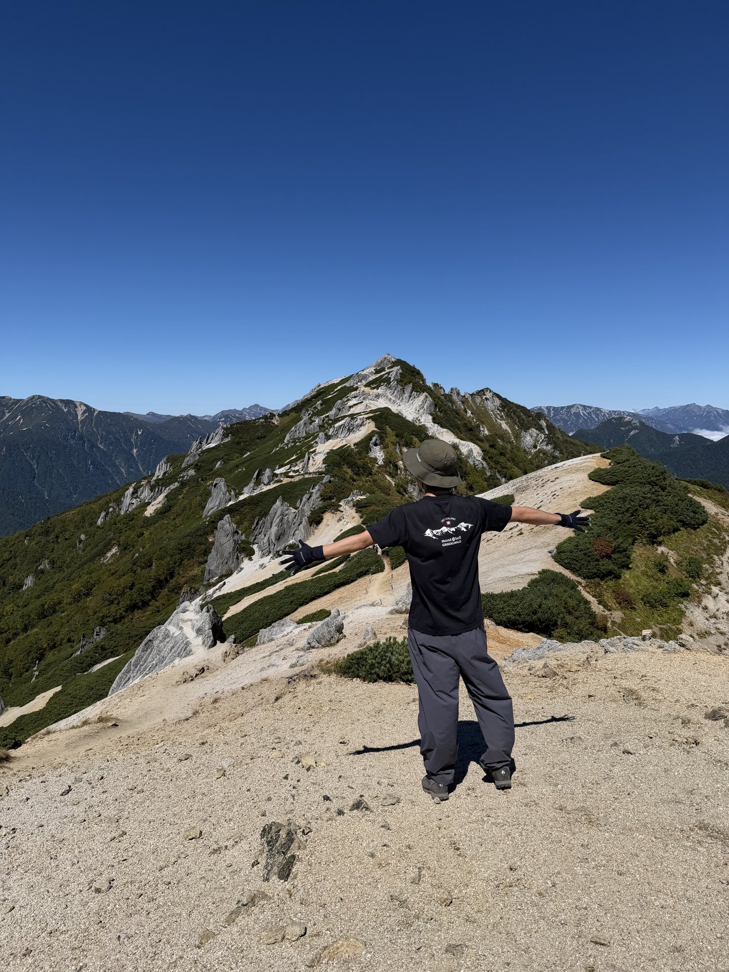 燕岳の白い花崗岩の稜線で両手を広げる登山者
